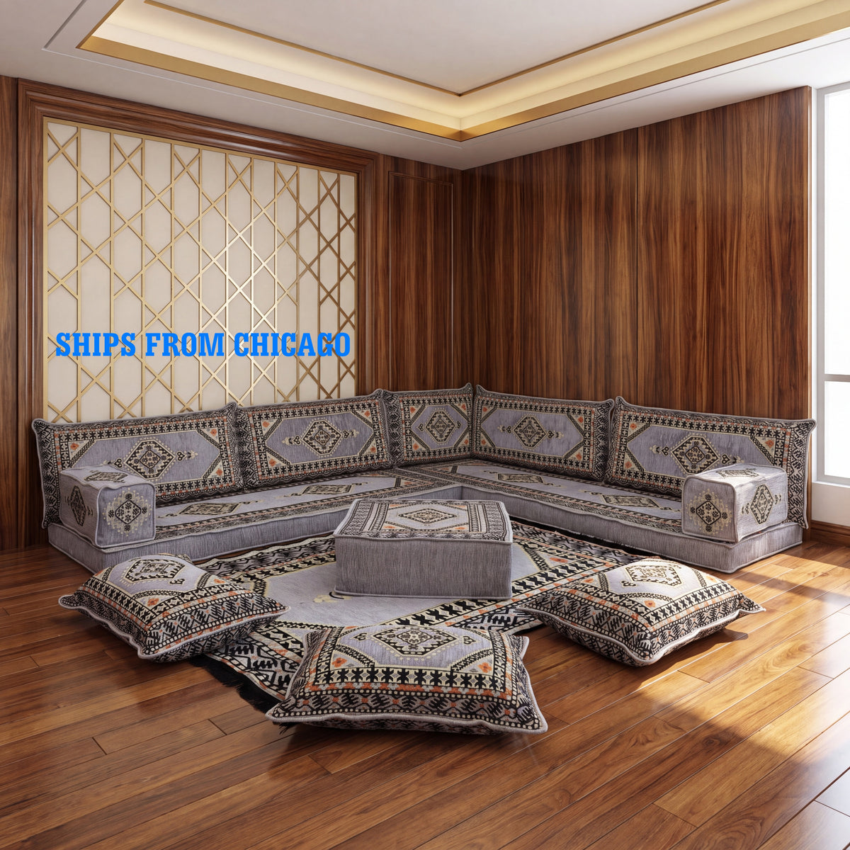 A Arabic-style modular upholstered gray floor seating sofa set arranged in a stone-walled living room. The set includes a low modular sectional sofa, matching armchair, ottoman, and several decorative throw pillows with geometric majlis patterns.