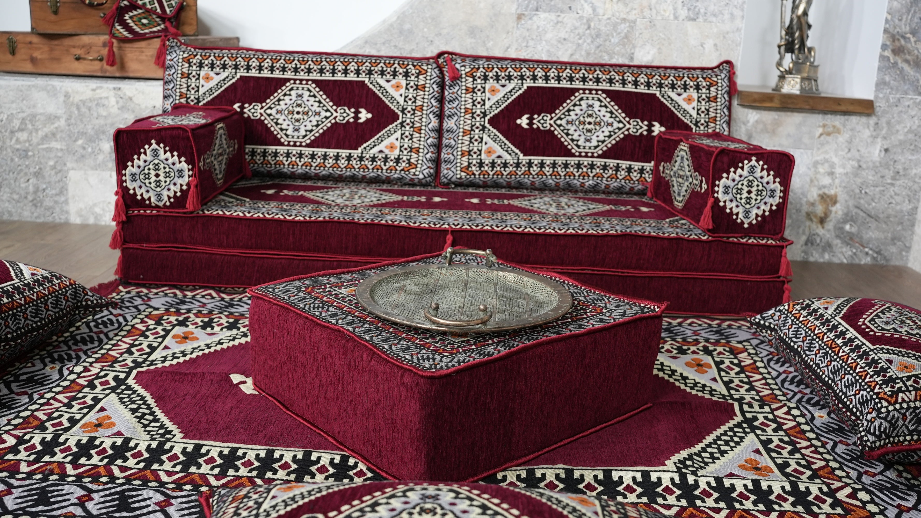 A traditional Turkish-style sofa upholstered in Burgundy Turkish Floor Sofa Set - 8 Inch Thick Palace Seating Modular Couch with Matching Rug, accompanied by a matching red ottoman and matching patterned rug.