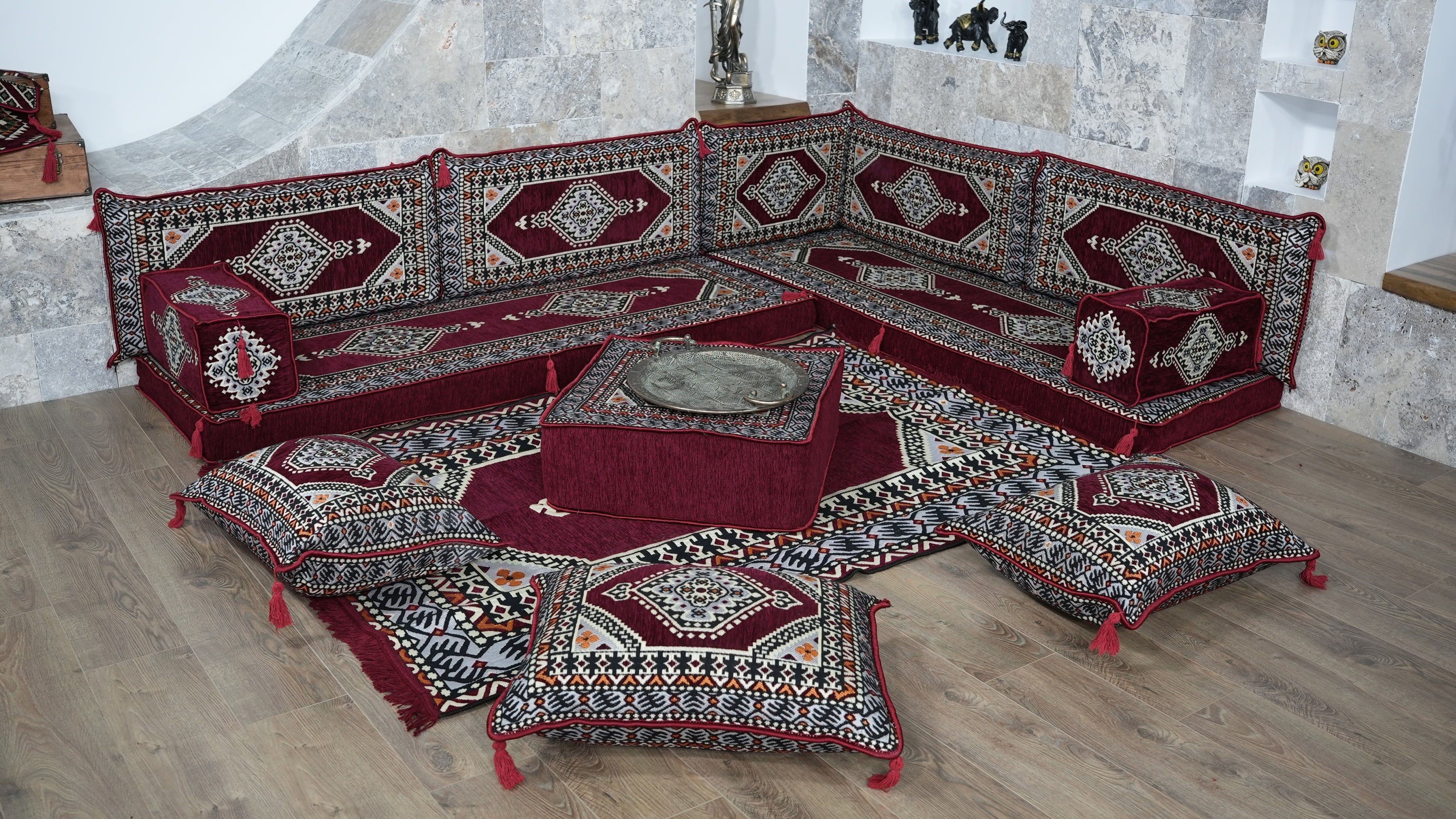 A modular L-shaped floor sofa set upholstered in deep red, burgundy with intricate white, and gold geometric patterns, accompanied by matching patterned floor cushions and a central low ottoman.