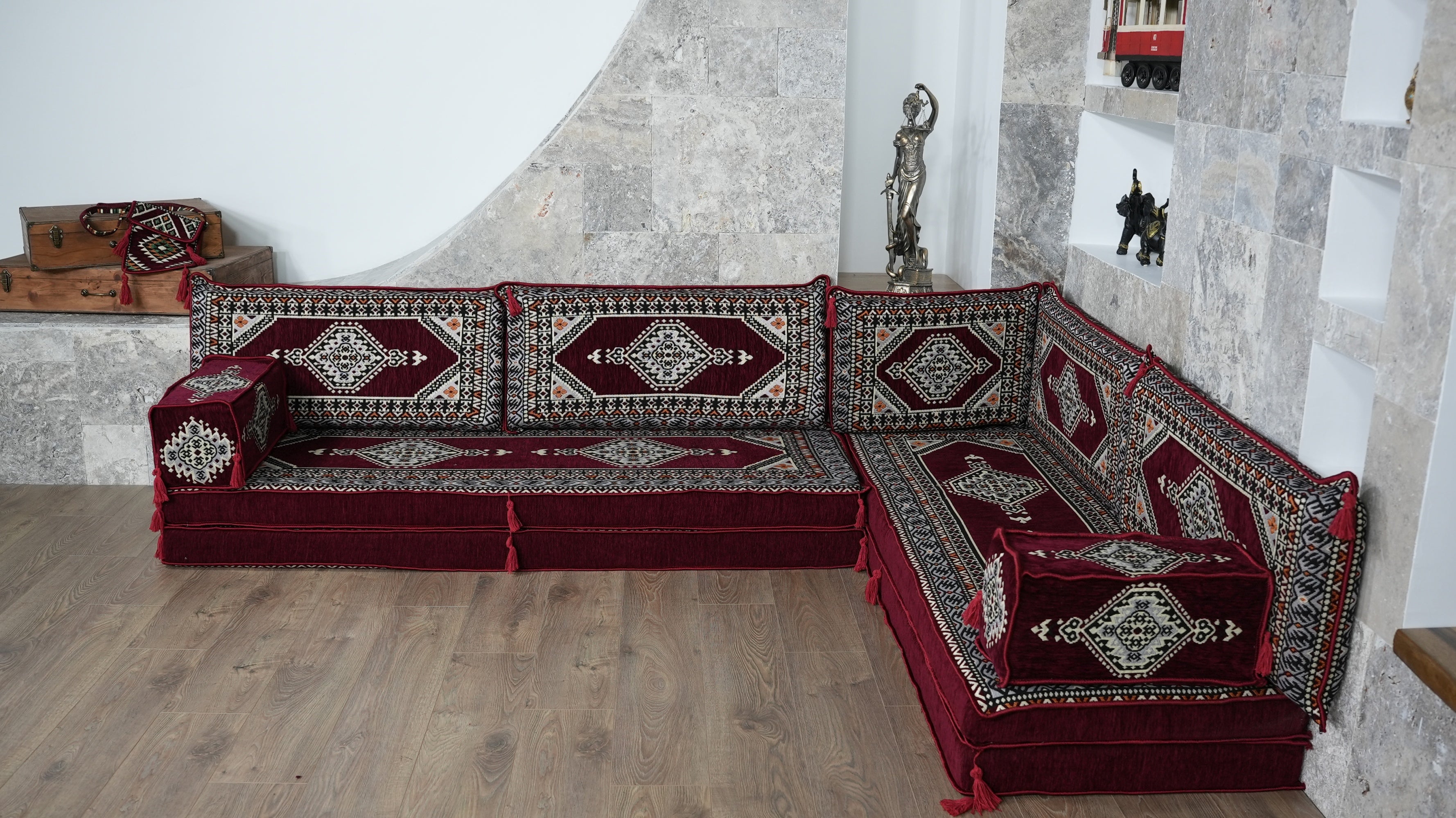 A traditional modular corner sectional sofa upholstered in deep burgundy velvet with intricate geometric and floral patterns in beige, black, and white, set in a room with stone walls and a light wood floor.