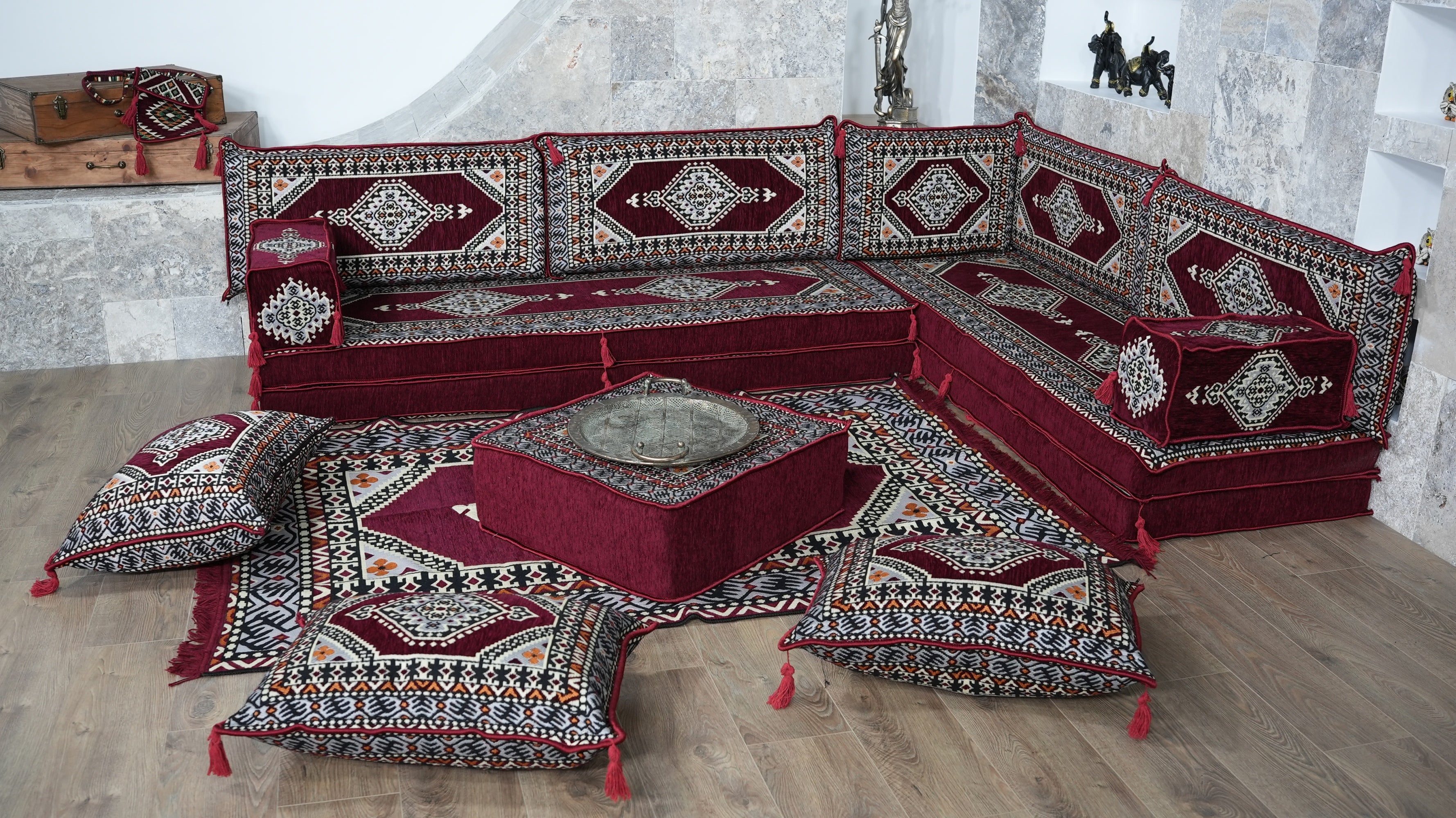 A traditional Turkish-style modular floor sofa set upholstered in deep red, burgundy with intricate geometric and arabic majlis patterns. The set includes multiple seat cushions, backrest cushions, and a central square ottoman on a matching patterned rug.