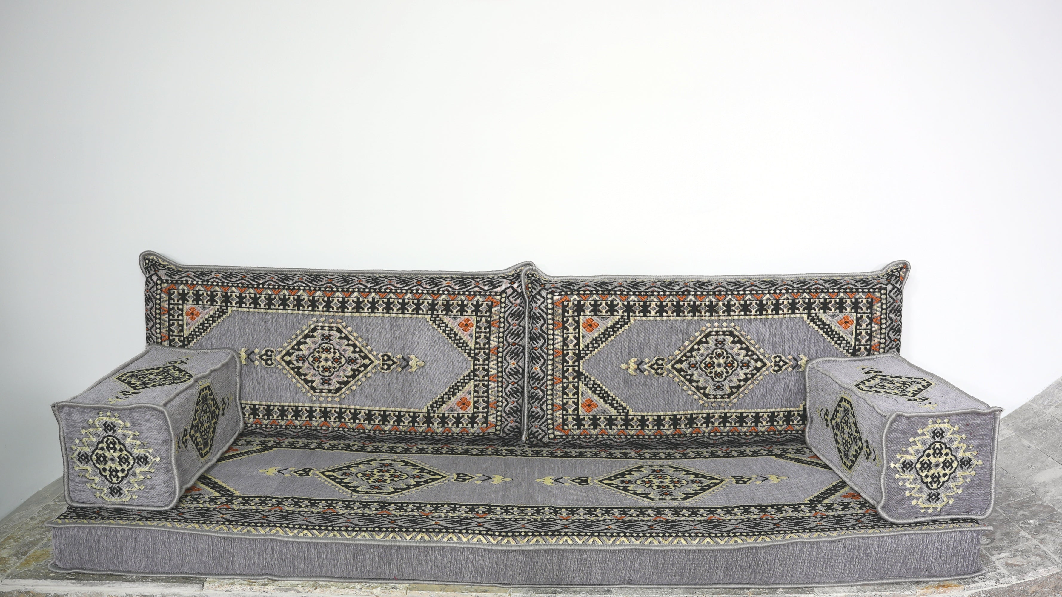 Turkish Floor Seating Loveseat. A low upholstered floor cushion with a gray base and matching back cushions, decorated with intricate geometric and tribal-style patterns in gray, black, beige, and orange.