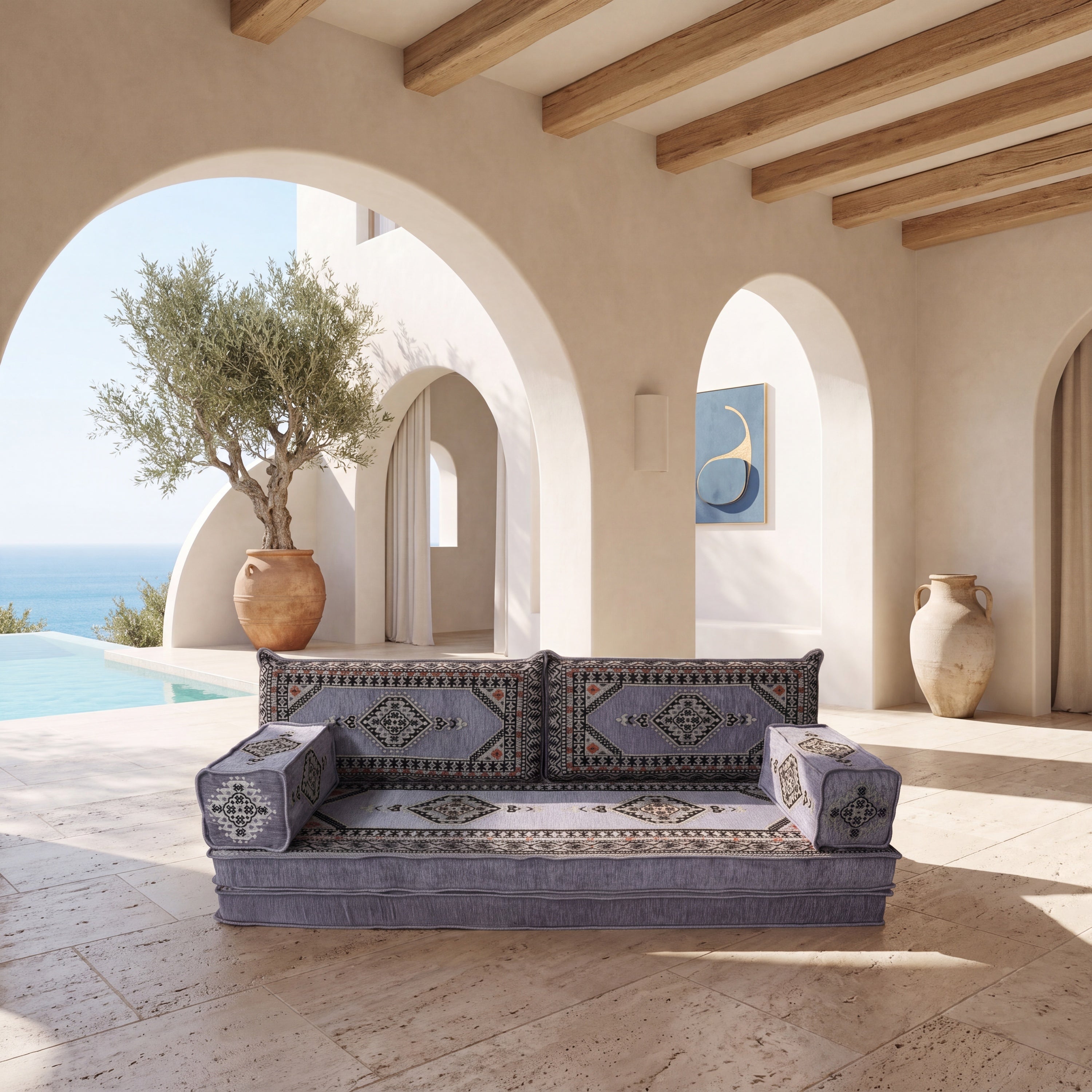 A low upholstered sofa with ornate geometric patterned cushions in muted gray placed in a sunlit Mediterranean-style patio setting.