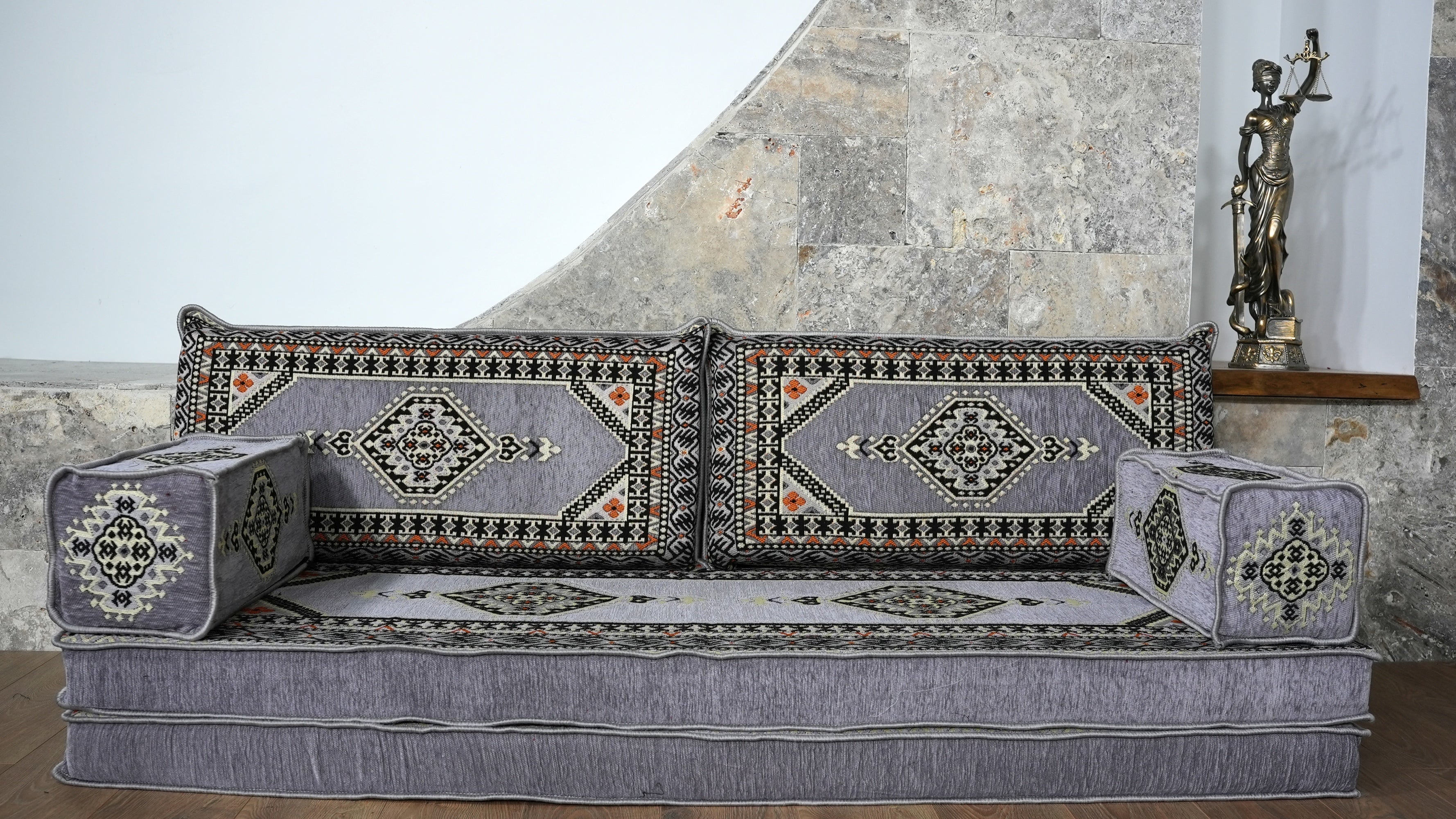 A low upholstered floor sofa with decorative Turkish and Arabic patterned cushions and a matching back seats and armrests.
