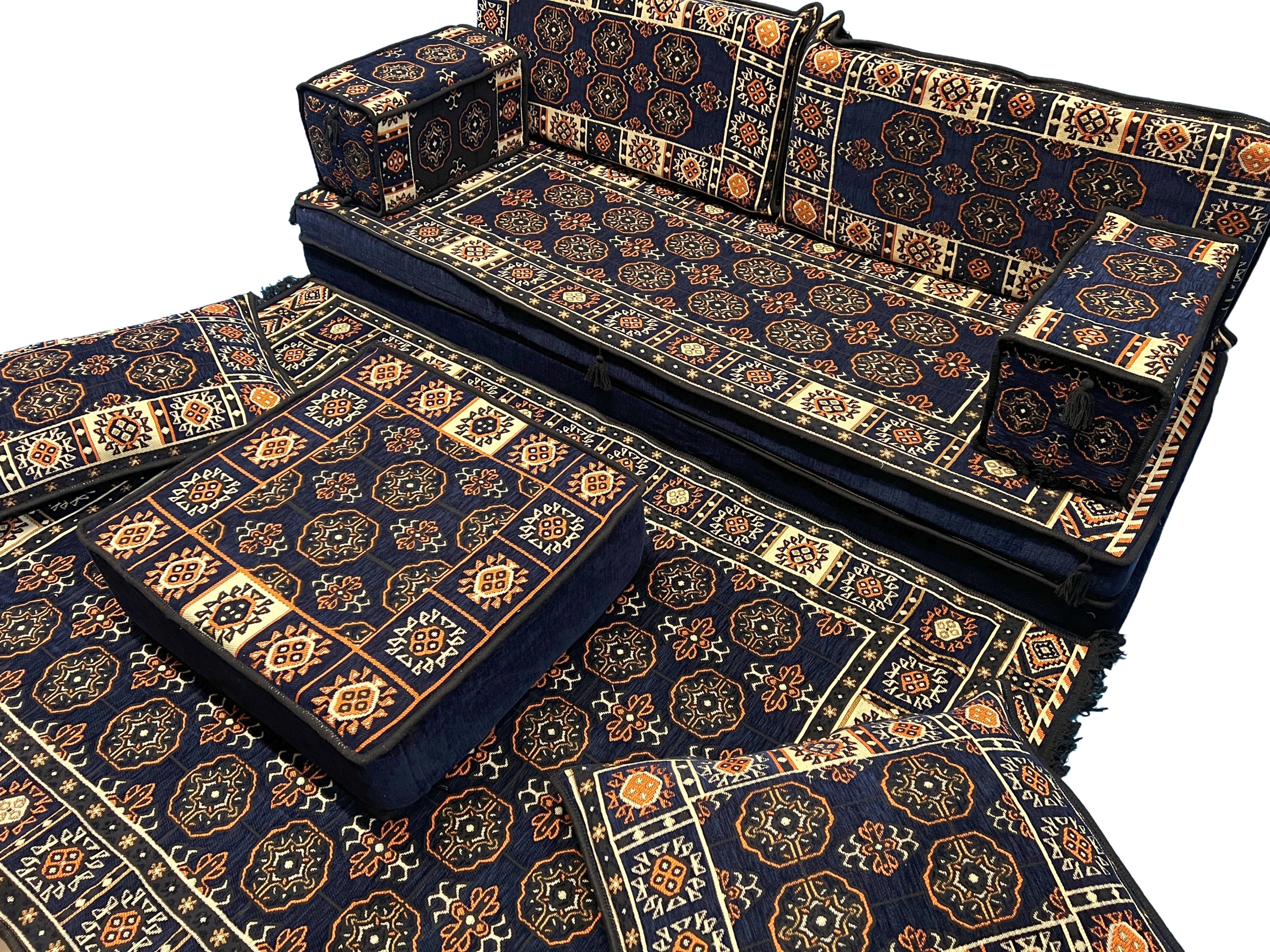 A set of patterned upholstered loveseat sofa majlis, including a loveseat, ottoman, and matching floor pillows and kilim rug.